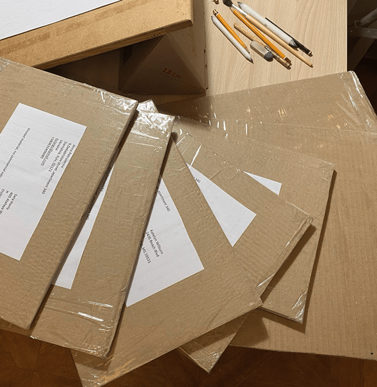 Pencil portraits are carefully packed in cardboard envelopes, placed on the table, and ready for shipping. The sturdy packaging ensures the artwork is well-protected during transit.