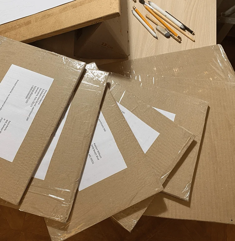 Pencil portraits are carefully packed in cardboard envelopes, placed on the table, and ready for shipping. The sturdy packaging ensures the artwork is well-protected during transit.