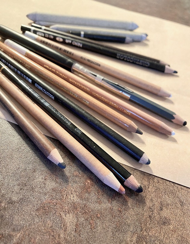 On the table, a close-up shows pastel pencils in warm brown tones, neatly arranged for ease of use. Just beyond, blending techniques can be seen, adding texture and depth to the artistic process.