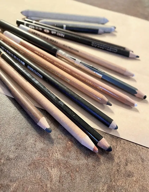 On the table, a close-up shows pastel pencils in warm brown tones, neatly arranged for ease of use. Just beyond, blending techniques can be seen, adding texture and depth to the artistic process.