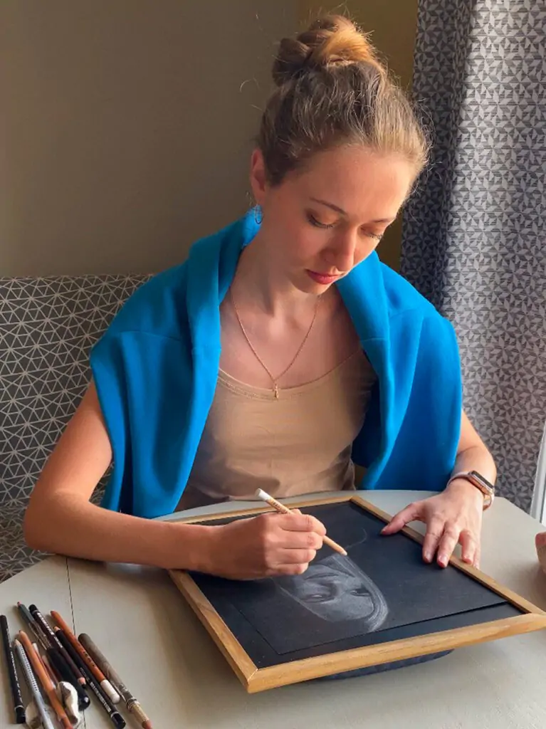 L’artiste Anneli de Anneli Studio dessine un portrait à la table avec des pastels.
