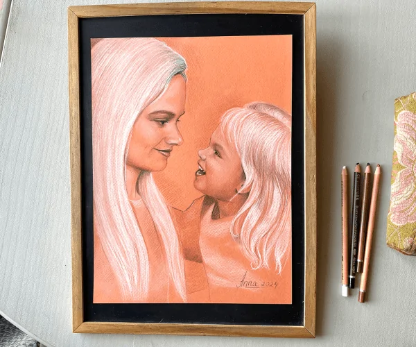 The portrait, created in pastel on toned peach paper, depicts a young mother and her three-year-old daughter looking at each other with sincere smiles. Both are joyful, with white hair that unites them. The portrait is done in several colors, creating a vibrant and warm atmosphere. Next to the portrait, four pastel pencils used for the artwork are neatly arranged.